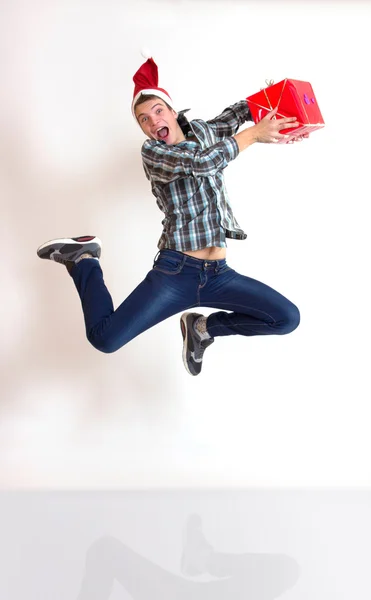 Young man in santa cap jumping with gifts — Stock Photo, Image