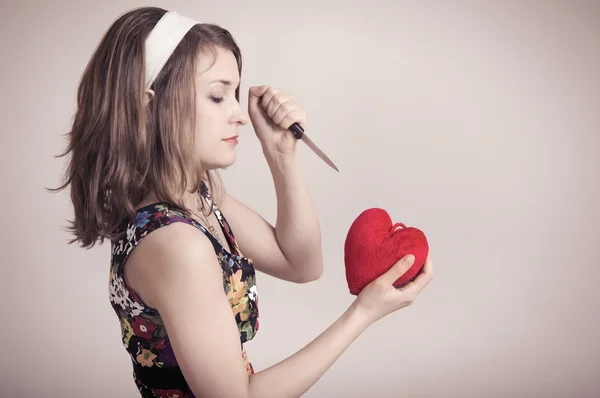 Woman cutting a toy heart with a knife — Stock Photo, Image