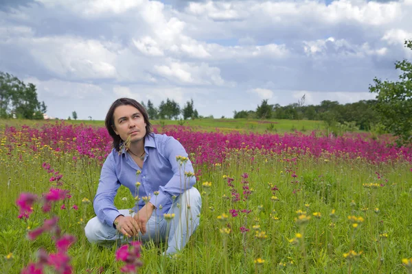 Mladý muž sedí na zelené louce — Stock fotografie