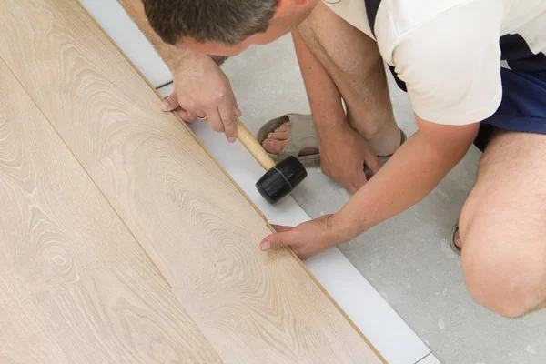 Δύο εργαζόμενοι συναρμολόγηση φυλλόμορφο πάτωμα χρησιμοποιώντας ένα σφυρί — Φωτογραφία Αρχείου