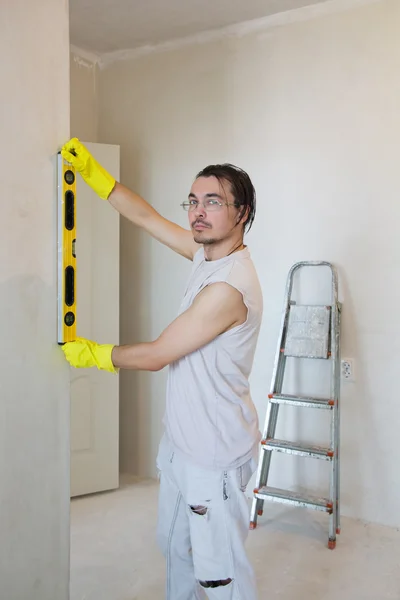 Jeune homme vérifiant le niveau du mur de la maison — Photo