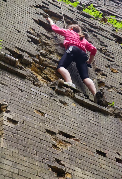 Young woman climbing up brick wall — Stock Photo, Image