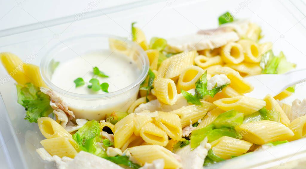 Penne pasta in a mayonnaise dressing with bacon pieces topped with parsley rubbed cooked chicken breast pieces, healthy salad in the plastic food box