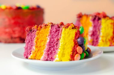 Gökkuşağı kutlama pastası, kremayla kaplanmış renkli sünger pastası ve gevrek bir şeker kabuğunda meyveli turta ile süslenmiş meyveli şekerle süslenmiş el pastası.