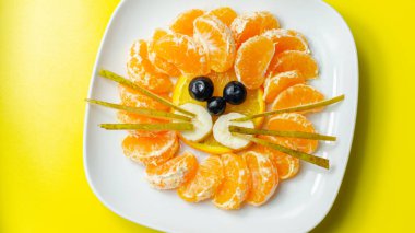 Taze meyve portakalı, mandalina, muz, üzüm ve armut yaratıcı bir şekilde servis edilir, aslan başı şeklinde meyveler, komik yiyecekler.