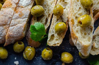 Zeytinle doldurulmuş baget, taze yeşil zeytin ve maydanozla kesilmiş, taş tabakta servis edilmiş, sağlıklı aperatif.