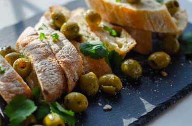 Zeytinle doldurulmuş baget, taze yeşil zeytin ve maydanozla kesilmiş, taş tabakta servis edilmiş, sağlıklı aperatif.