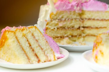 Nemli madeira süngeri, erik ve ahududu reçeli katmanlı, beyaz ve pembe donlarla kaplı, beyaz çikolata süslemeleri ile süslenmiş, doğum günü pastası