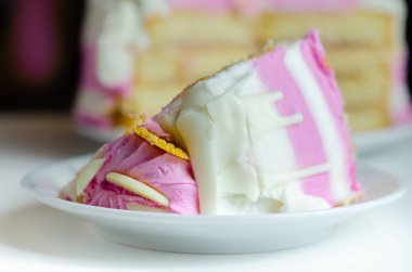 Nemli madeira süngeri, erik ve ahududu reçeli katmanlı, beyaz ve pembe donlarla kaplı, beyaz çikolata süslemeleri ile süslenmiş, doğum günü pastası