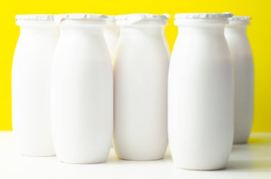 Sarı zemin üzerinde beyaz plastik yoğurt şişeleri, süt ürünleri için tipik ambalaj, ürün şişesi