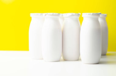 Sarı zemin üzerinde beyaz plastik yoğurt şişeleri, süt ürünleri için tipik ambalaj, ürün şişesi