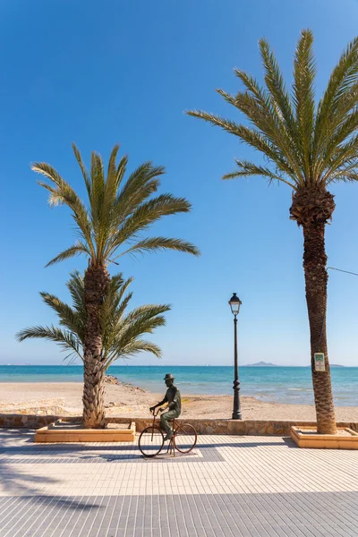 LOS ALCAZARES, SPAIN - 25 Şubat 2019 Los Alcazares şehri 50 yılı aşkın süredir popüler bir aktör tarafından seçilen bir tatil beldesiydi, ölümünden sonra kendisine ithaf edilen bir heykel, onu tipik bir resimde, bisiklette ve şapkada tasvir eder.