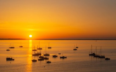 Gemiler, tekneler ve yatlar körfezde demirlemiş güneşin doğuşuna karşı, cennet gibi bir görüntü