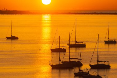 Gemiler, tekneler ve yatlar körfezde demirlemiş güneşin doğuşuna karşı, cennet gibi bir görüntü