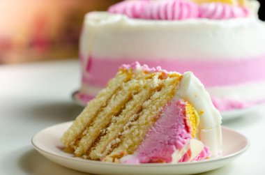 Nemli madeira süngeri, erik ve ahududu reçeli katmanlı, beyaz ve pembe donlarla kaplı, beyaz çikolata süslemeleri ile süslenmiş, doğum günü pastası