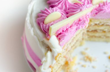 Nemli madeira süngeri, erik ve ahududu reçeli katmanlı, beyaz ve pembe donlarla kaplı, beyaz çikolata süslemeleri ile süslenmiş, doğum günü pastası