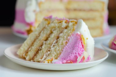 Nemli madeira süngeri, erik ve ahududu reçeli katmanlı, beyaz ve pembe donlarla kaplı, beyaz çikolata süslemeleri ile süslenmiş, doğum günü pastası