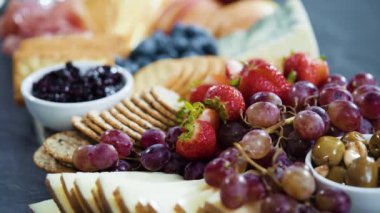 Aperatif olarak sunulan tahtanın üzerinde gurme peyniri, kraker ve meyve var..