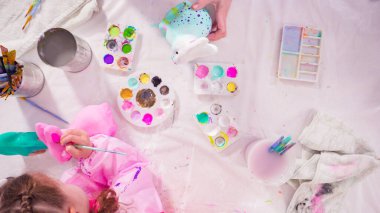 Düz yatıyordu. Küçük kız evde eğitim projesi için akrilik boyayla heykelcikler boyuyor..