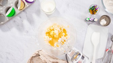 Düz yatıyordu. Adım adım. Vanilyalı Mardi Gras kekleri pişirmek için karışımı elektrikli mikserle karıştırıyorum..