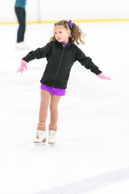 Küçük kız buz pateni pistinde artistik patinaj yapıyor..