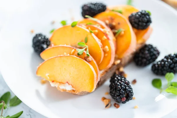 Peach ricotta toast garnished with blackberries on a white plate.