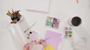 Evde akrilik boyalı bir sanat projesi üzerinde çalışan küçük bir kız..