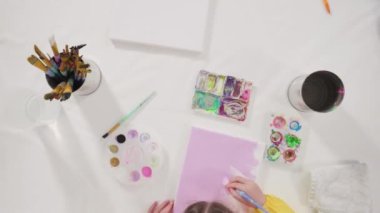 Evde akrilik boyalı bir sanat projesi üzerinde çalışan küçük bir kız..