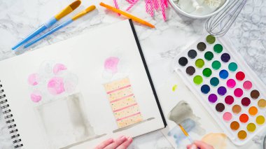 Düz yatıyordu. Baker suluboyalı bir doğum günü pastası çiziyor..