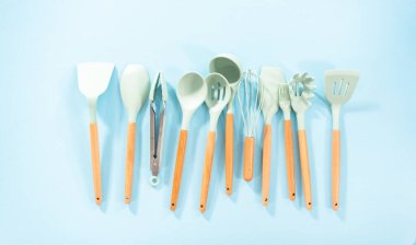 Düz yatıyordu. Mavi arka planda ahşap saplı yeni mavi silikon mutfak aletleri..