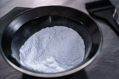 Siyah arka planda siyah plastik bir kasede saç boyası tozu..