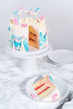 Deniz kızı temalı 3 katlı vanilyalı pasta dilimi. Çikolatalı deniz kızı kuyruğu ve beyaz tabakta deniz kabukları..