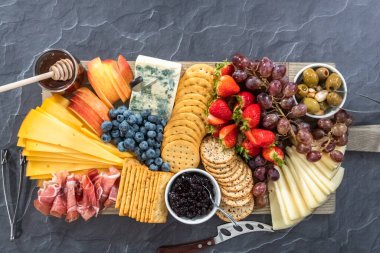 Düz yatıyordu. Aperatif olarak sunulan tahtanın üzerinde gurme peyniri, kraker ve meyve var..