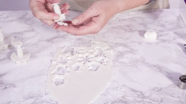 Adım adım. Mermer tezgahın üzerindeki beyaz fondanla kar tanelerini keserek..