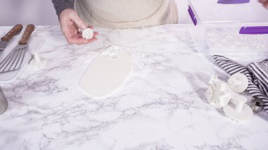 Adım adım. Mermer tezgahın üzerindeki beyaz fondanla kar tanelerini keserek..