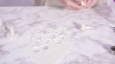 Adım adım. Mermer tezgahın üzerindeki beyaz fondanla kar tanelerini keserek..