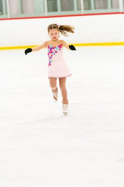 Küçük kız buz pateni pistinde artistik patinaj yapıyor..