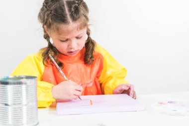 Evde akrilik boyalı bir sanat projesi üzerinde çalışan küçük bir kız..