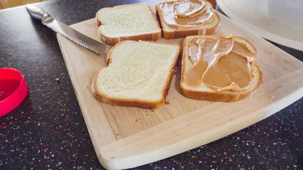 Preparing peanut butter and jelly sandwich on a wood cutting board.