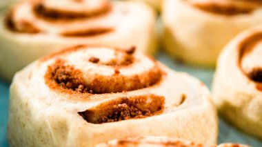 Fırınlanmamış tarçınlı çörekler mavi bir tavada.