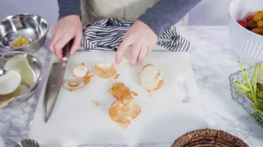 Cutting onion on a white cutting board to make a one-pot pasta recipe.