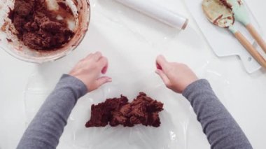 Wrapping cookie dough into the plastic wrap to bake chocolate cookies.