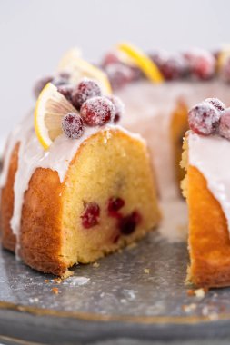 Sliced lemon cranberry bundt cake decorated with sugar cranberries and lemon wedges on a cake stand. clipart