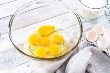 Ahşap bir masada yumurtalı ekmek hazırlamak için cam karıştırma kabındaki malzemeler..