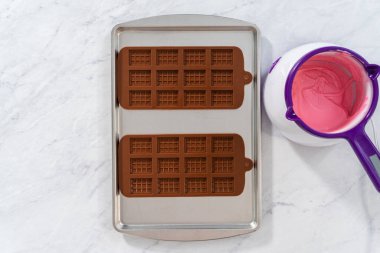 Flat lay. Filling silicone chocolate mold with melted chocolate to make mini pink chocolates.