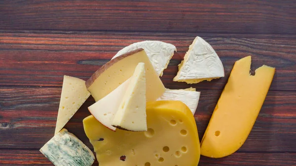 Flat lay. Large wedges of gourmet cheese on a rustic wood background.