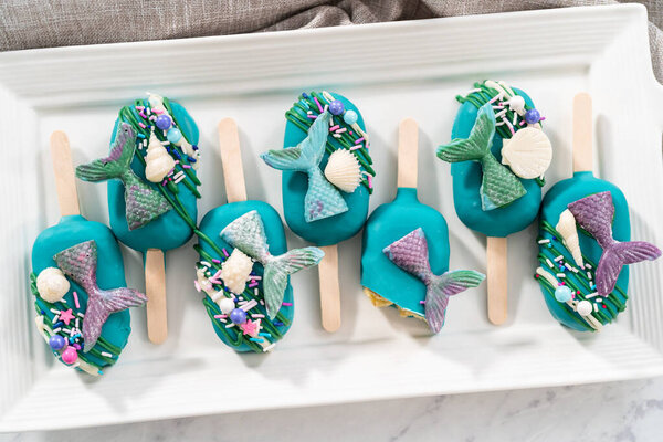 Mermaid cakesicles with drizzled chocolate, chocolate mermaid tails, seashells, and sprinkles.
