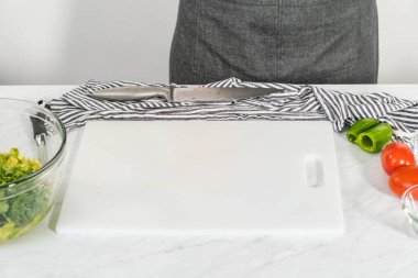 Klasik guacamole sosu yapmak için beyaz kesim tahtasındaki malzemeleri kesiyorum..