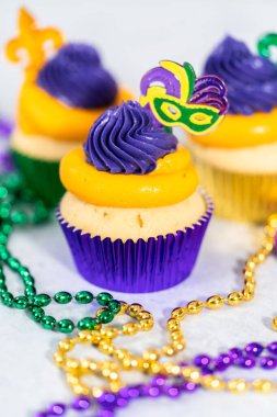 Mardi Gras vanilyalı kekler folyo kaplarda ve İtalyan tereyağlı kremayla süslenmiş..
