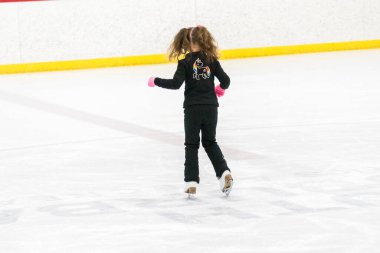 Küçük kız buz pistinde artistik patinaj yapıyor..